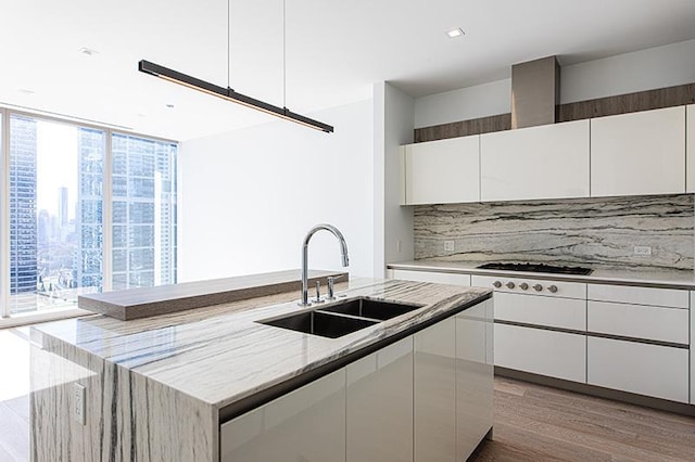 kitchen featuring a sink, white cabinetry, light wood-type flooring, tasteful backsplash, and an island with sink