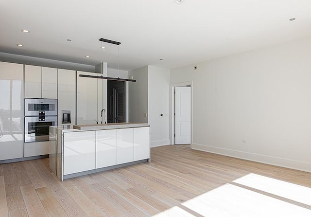 kitchen featuring double oven, a sink, light wood-style floors, white cabinets, and modern cabinets