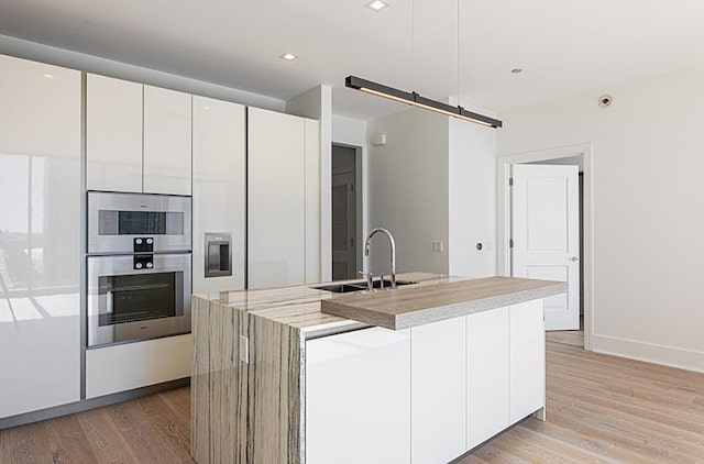 kitchen featuring light wood finished floors, a barn door, stainless steel double oven, white cabinets, and a sink