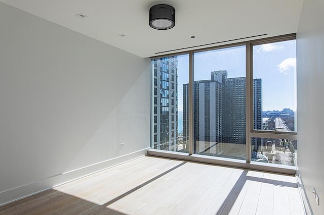 spare room with a view of city, baseboards, wood finished floors, and floor to ceiling windows