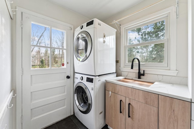 laundry room featuring stacked washer and dryer, a sink, cabinet space, and dark tile patterned floors