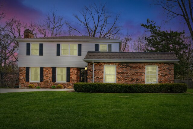 view of front of home with fence, a chimney, brick siding, and a front lawn
