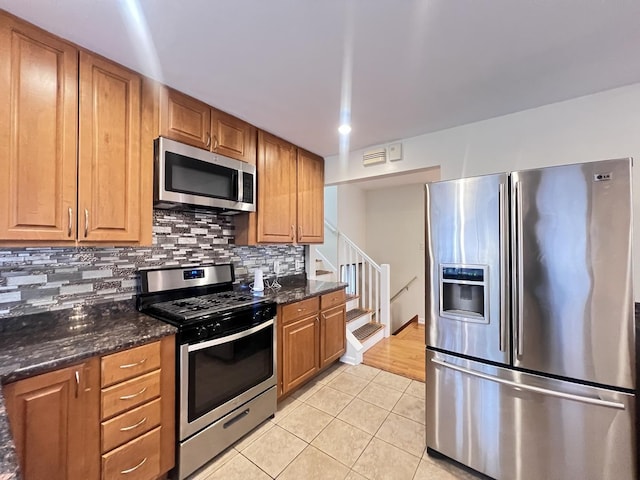 kitchen with appliances with stainless steel finishes, decorative backsplash, dark stone countertops, and light tile patterned flooring