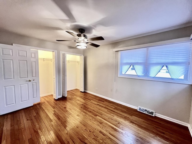 unfurnished bedroom with baseboards, visible vents, ceiling fan, wood finished floors, and multiple closets