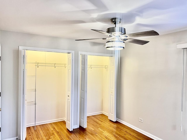 unfurnished bedroom with light wood-type flooring, ceiling fan, baseboards, and two closets