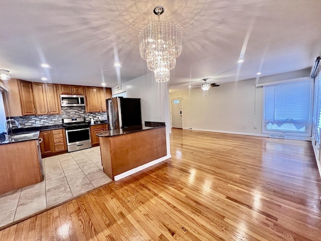 kitchen with tasteful backsplash, appliances with stainless steel finishes, brown cabinets, light wood-type flooring, and a sink