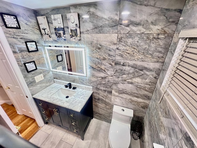 bathroom featuring wood finished floors, vanity, toilet, and tile walls