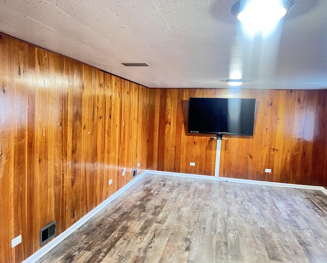 unfurnished living room featuring visible vents, wood walls, baseboards, and wood finished floors