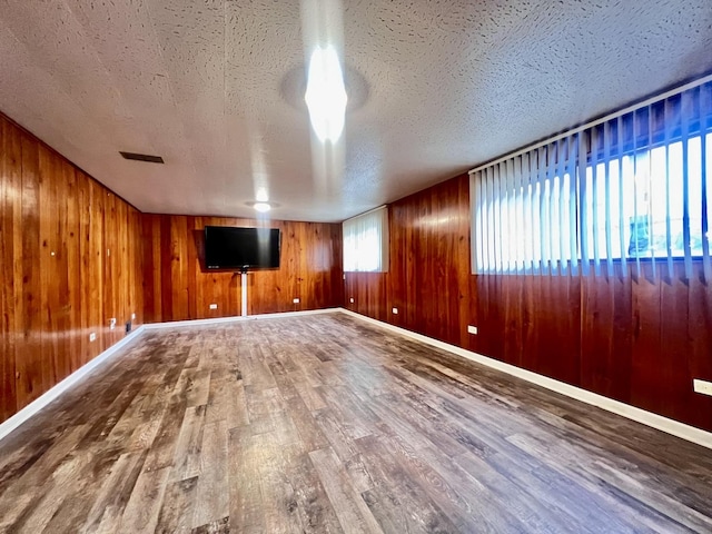 unfurnished living room with visible vents, a textured ceiling, baseboards, and wood finished floors