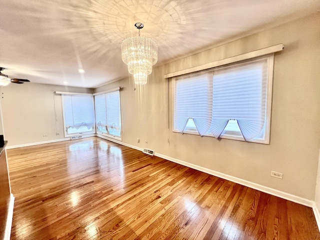 unfurnished room with hardwood / wood-style flooring, baseboards, visible vents, and ceiling fan with notable chandelier