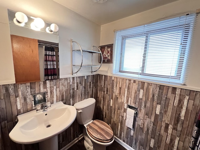 bathroom featuring wooden walls, wainscoting, toilet, a shower with curtain, and a sink