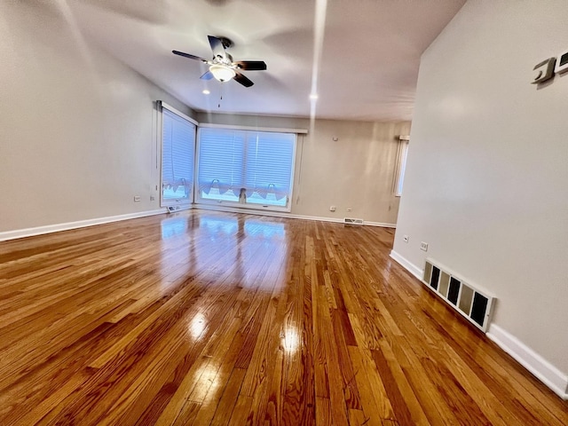 empty room with wood-type flooring, visible vents, and baseboards