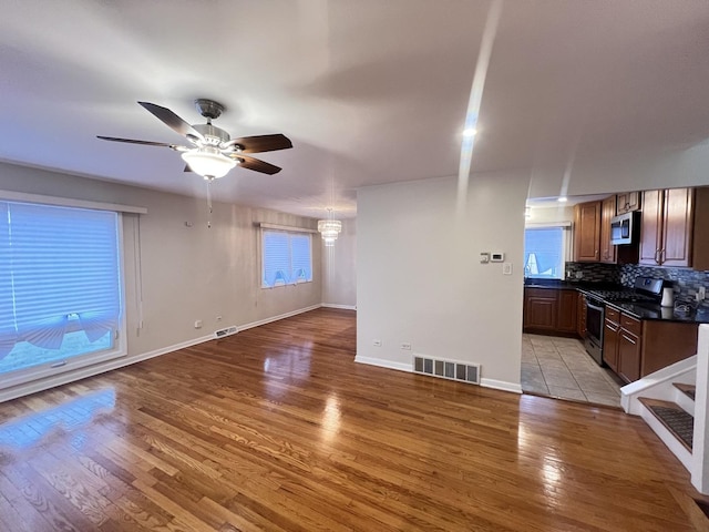 unfurnished living room featuring a wealth of natural light, light wood-type flooring, visible vents, and a ceiling fan