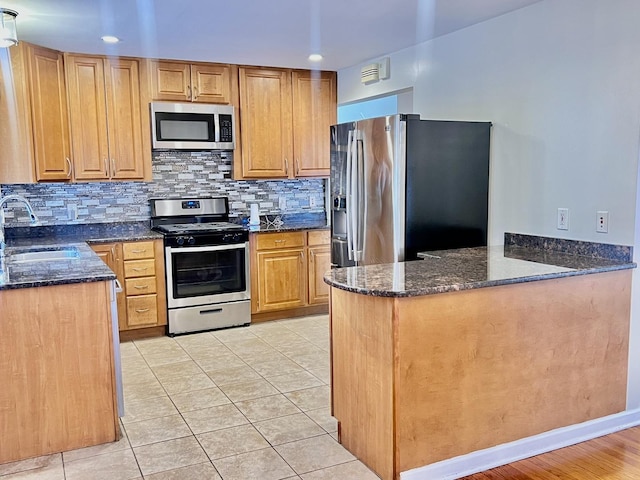 kitchen featuring backsplash, dark stone countertops, stainless steel appliances, and a sink