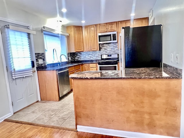 kitchen with light tile patterned floors, appliances with stainless steel finishes, backsplash, dark stone countertops, and a sink