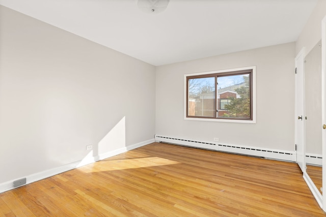 unfurnished room with light wood-style flooring, a baseboard heating unit, and baseboards