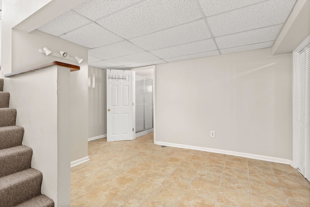 finished below grade area featuring a paneled ceiling, baseboards, and stairs