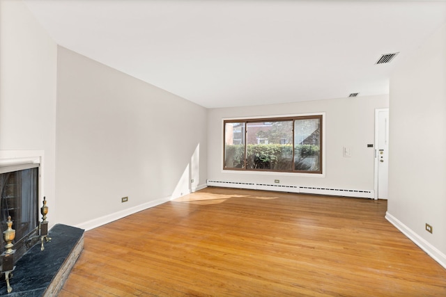 living room featuring visible vents, a fireplace with raised hearth, a baseboard heating unit, light wood-type flooring, and baseboards