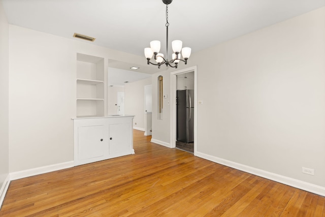 unfurnished dining area with baseboards, visible vents, built in features, light wood-style floors, and a chandelier