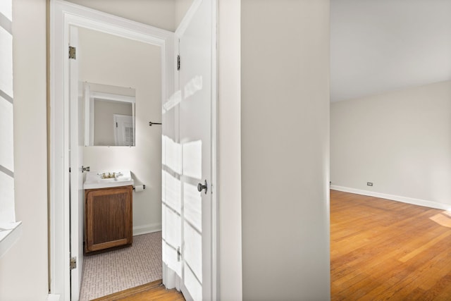 hallway with light wood-type flooring, a sink, and baseboards