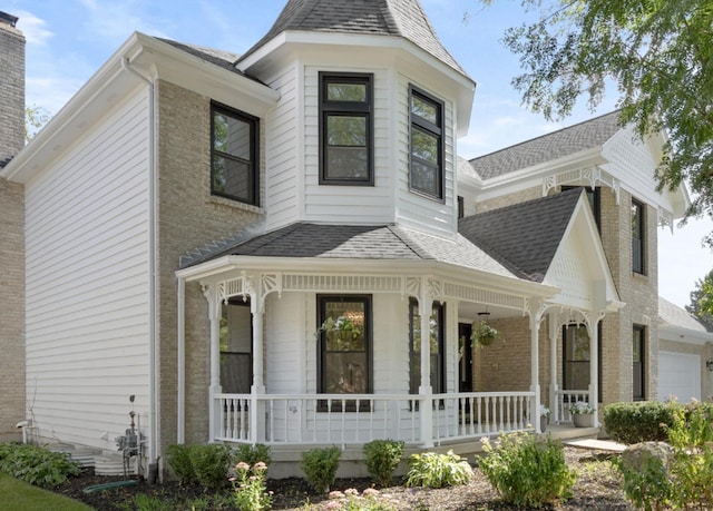 victorian-style house with covered porch, roof with shingles, a chimney, and brick siding