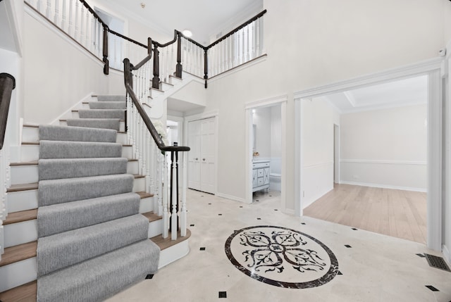 foyer with a high ceiling, visible vents, baseboards, stairway, and crown molding