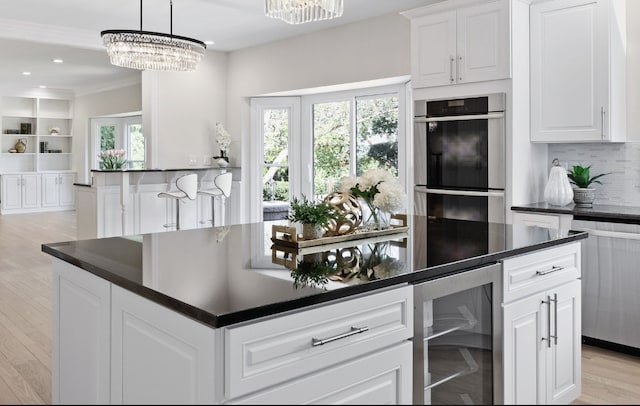 kitchen featuring beverage cooler, double oven, dark countertops, and light wood-style floors