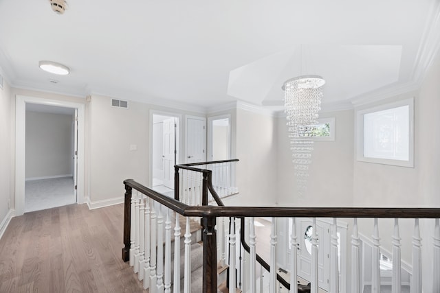 hallway featuring baseboards, visible vents, wood finished floors, crown molding, and an upstairs landing