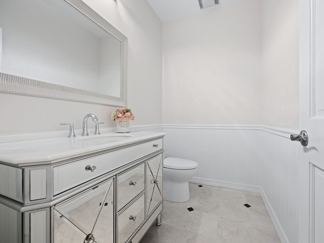 bathroom with toilet, a wainscoted wall, visible vents, and vanity