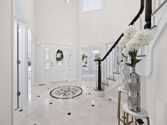 foyer with a towering ceiling, marble finish floor, baseboards, and stairway