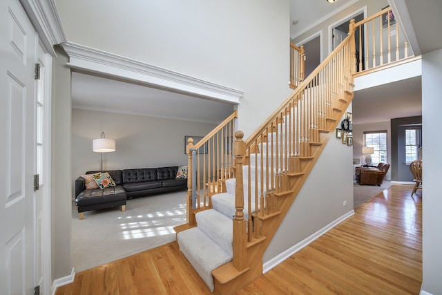 stairs featuring a high ceiling, crown molding, baseboards, and wood finished floors