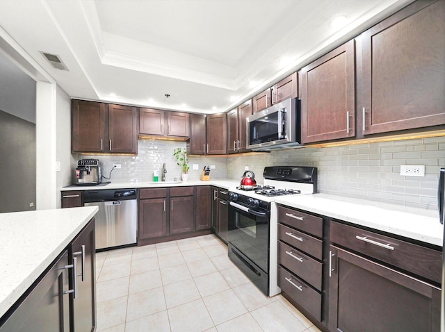 kitchen with a raised ceiling, light countertops, appliances with stainless steel finishes, and a sink