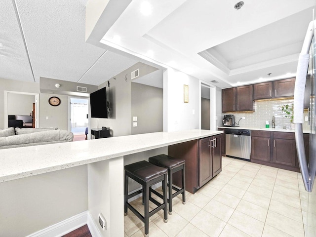 kitchen featuring visible vents, open floor plan, stainless steel appliances, a raised ceiling, and dark brown cabinets