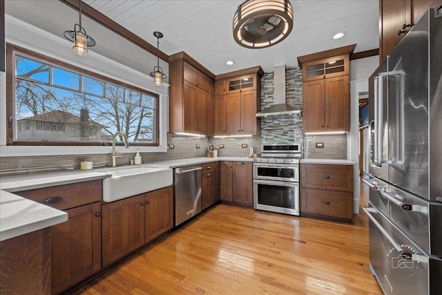 kitchen with a sink, stainless steel appliances, wall chimney exhaust hood, light countertops, and decorative backsplash