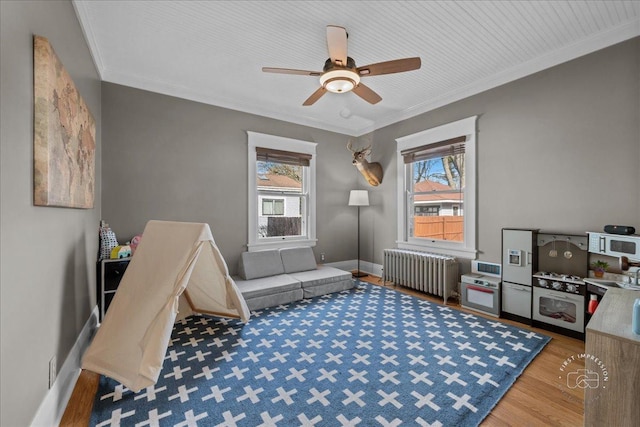 recreation room featuring a healthy amount of sunlight, crown molding, and radiator heating unit