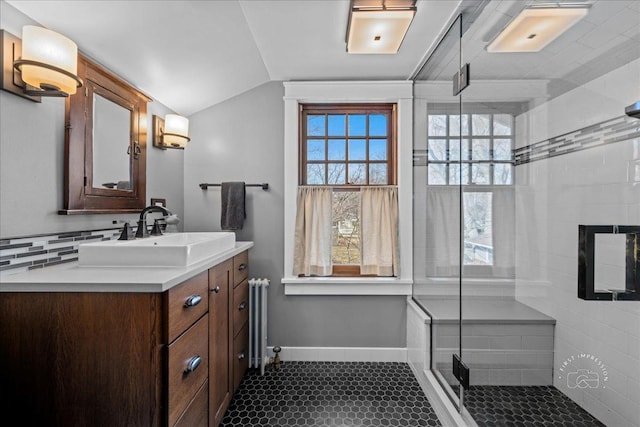 bathroom with radiator, a shower stall, baseboards, vanity, and vaulted ceiling