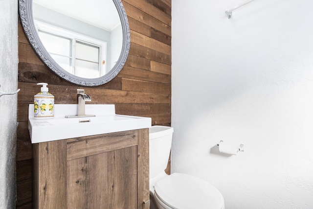 bathroom featuring wooden walls, toilet, and vanity