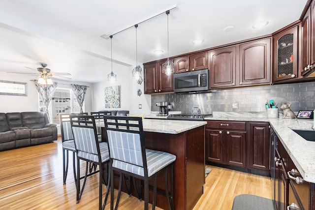 kitchen featuring tasteful backsplash, stainless steel microwave, light stone countertops, light wood-type flooring, and a kitchen bar