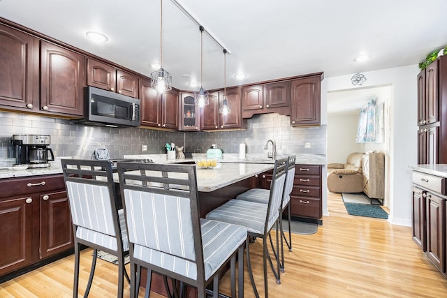 kitchen featuring stainless steel microwave, light wood-style floors, backsplash, and dark brown cabinetry