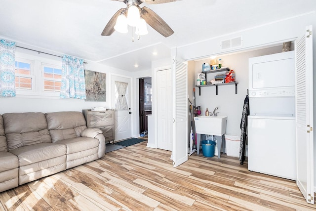 living area featuring stacked washer and dryer, a ceiling fan, visible vents, and light wood-type flooring