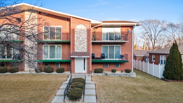 view of front of home featuring a balcony, a front yard, fence, and brick siding