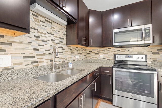 kitchen featuring decorative backsplash, light stone counters, appliances with stainless steel finishes, dark brown cabinets, and a sink