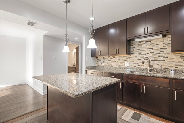 kitchen with light stone counters, light wood-style flooring, a sink, visible vents, and tasteful backsplash