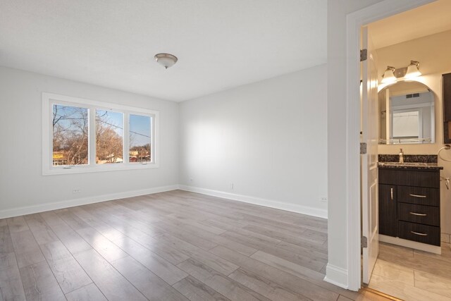 unfurnished bedroom featuring connected bathroom, light wood-style flooring, and baseboards