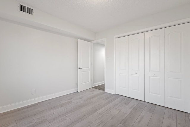 unfurnished bedroom featuring a textured ceiling, wood finished floors, visible vents, baseboards, and a closet