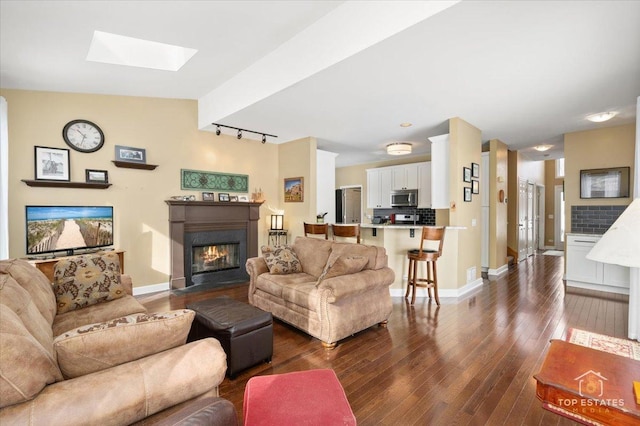 living area featuring baseboards, a skylight, a fireplace with flush hearth, dark wood-type flooring, and rail lighting