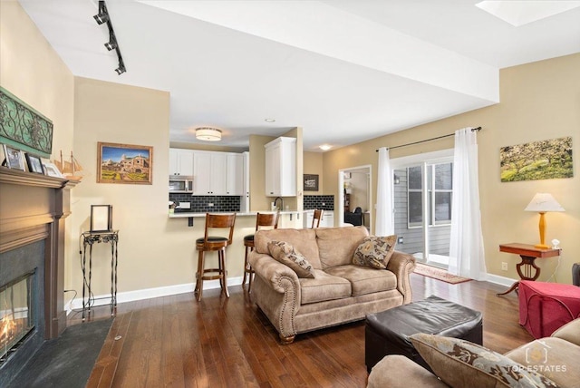 living room featuring dark wood-style floors, a glass covered fireplace, track lighting, and baseboards