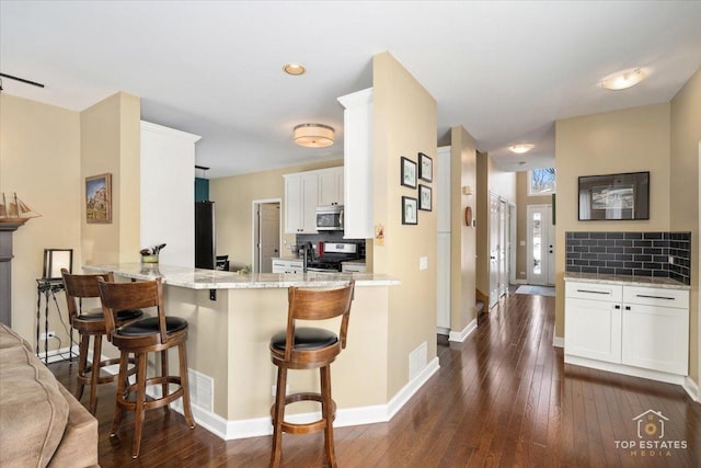 kitchen with stainless steel appliances, backsplash, white cabinets, and dark wood finished floors