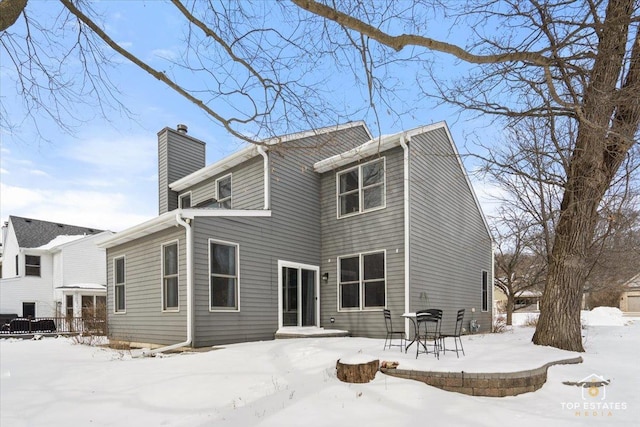 snow covered house with a patio area and a chimney