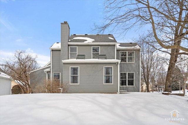 snow covered back of property with a chimney